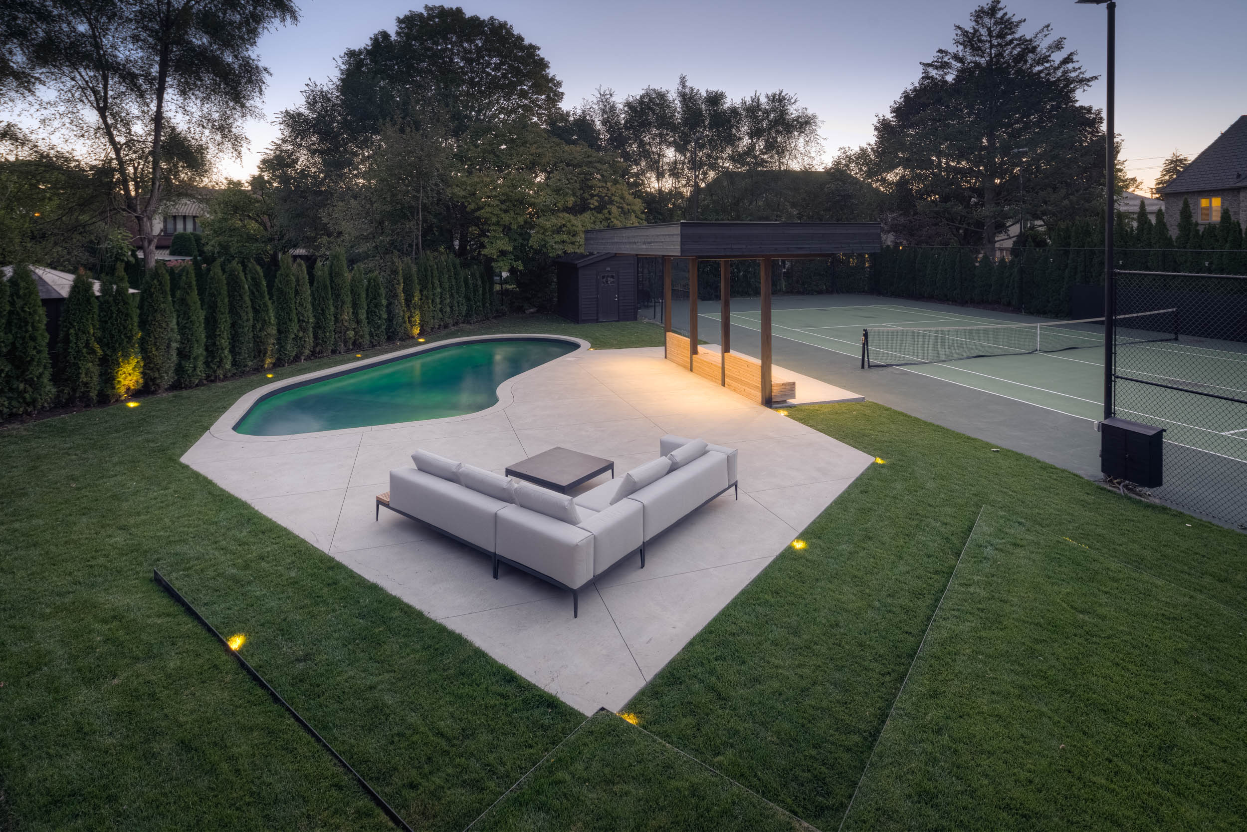 View of residential backyard with pool, tennis courts and outdoor seating. 