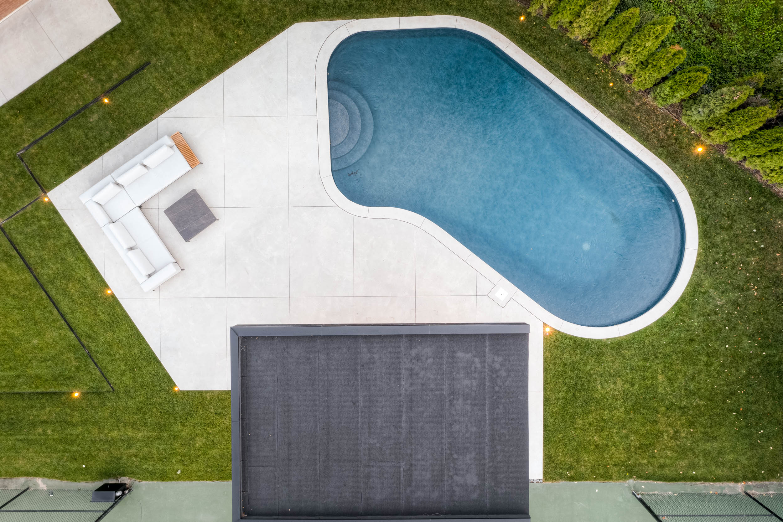 Overhead view of organic shaped pool with concrete decking and seating area. 