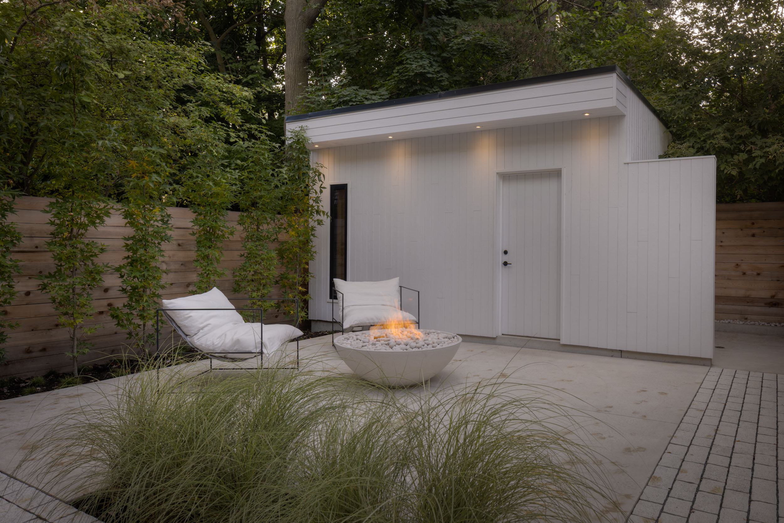Small backyard patio with modern fence, firetable, seating and white shed.