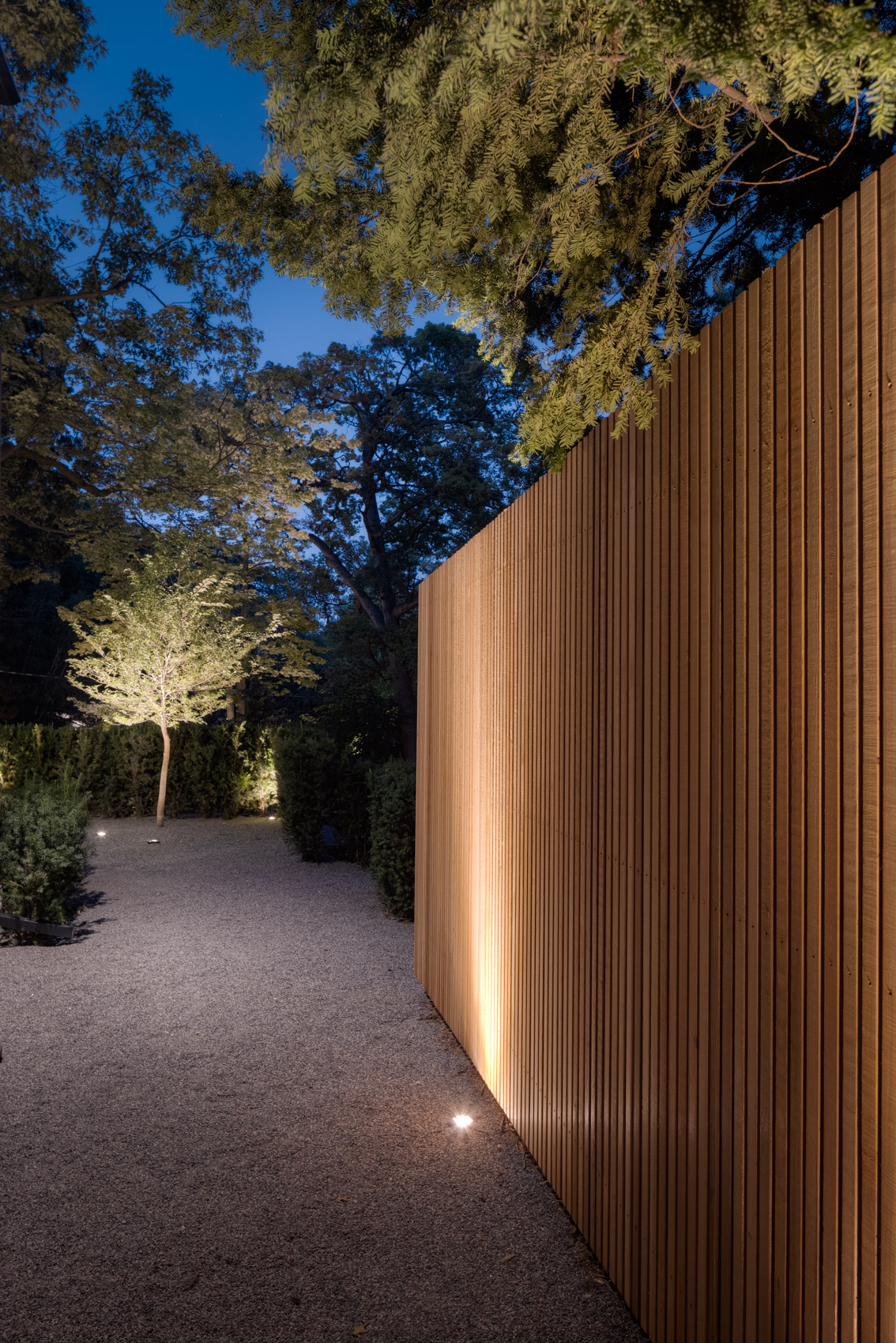 Landscape lighting featuring modern fencing and pebble walkway. 